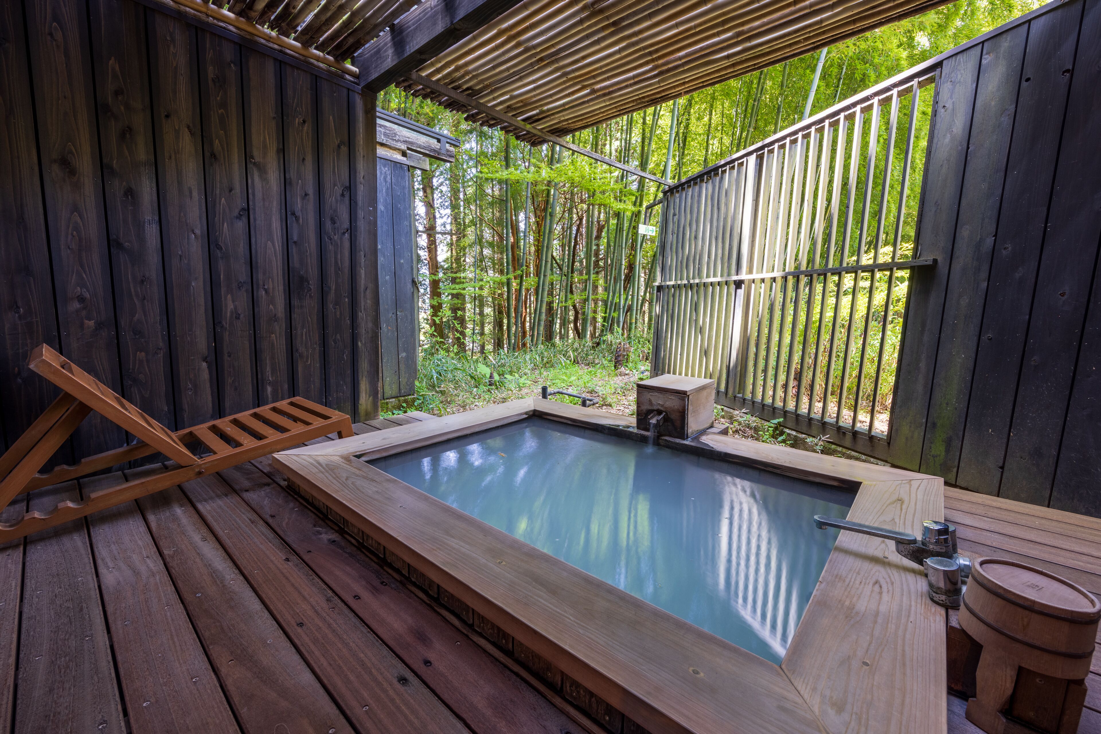 A wooden deck with a hot tub, surrounded by bamboo and a wooden fence.