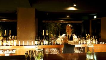 A bar area with a bartender preparing drinks, shelves with bottles, glasses, and a decorative plant in a glass container.