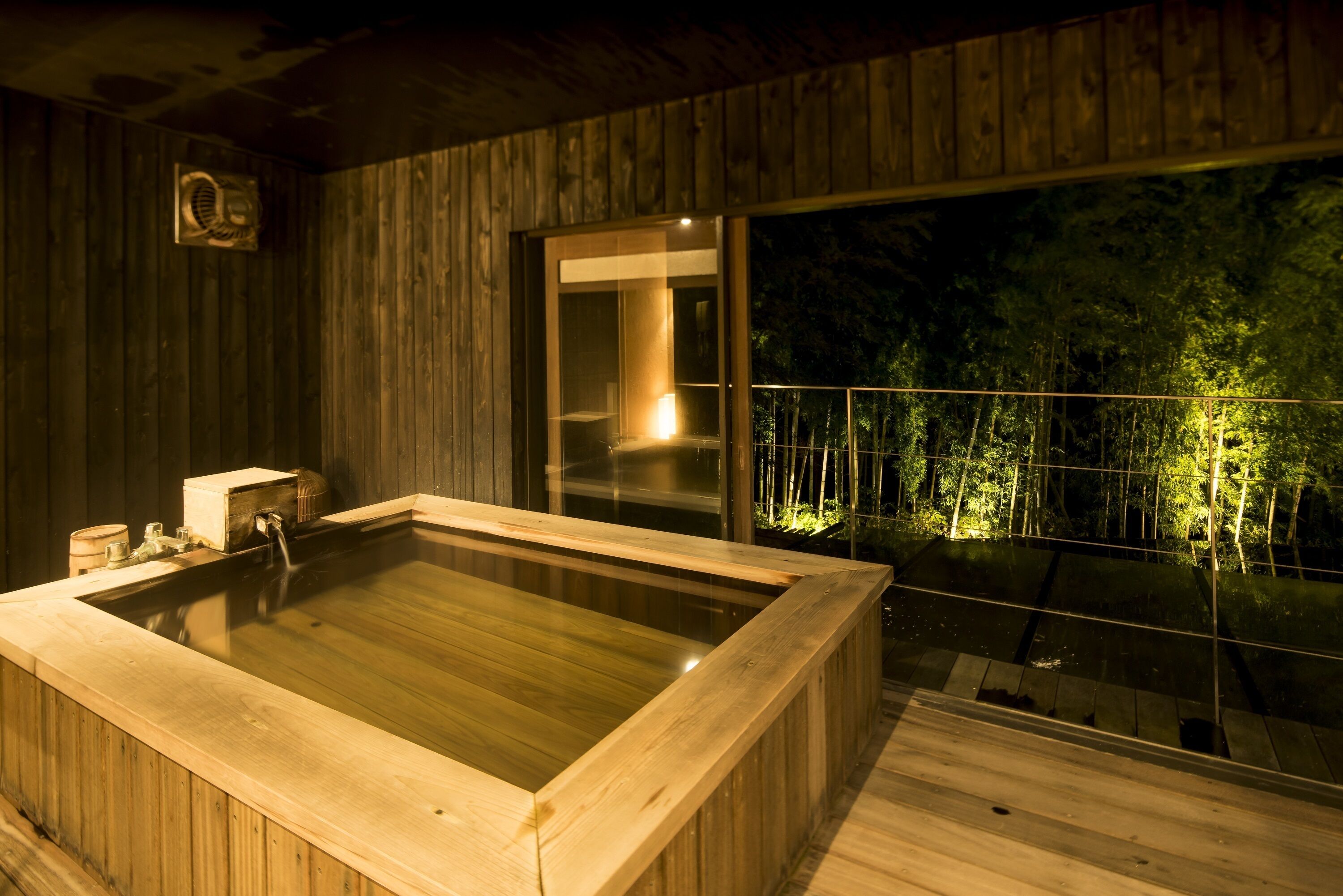 Una bañera de hidromasaje de madera con vistas a un balcón y árboles.