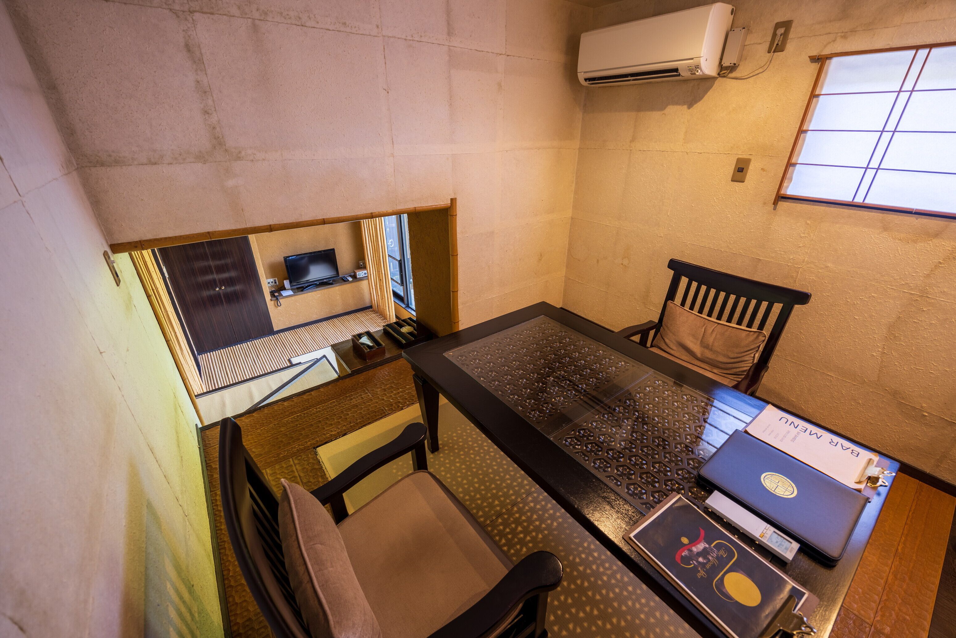 Een compacte hotelkamer met een klein kitchenette, een enkel bed, een raam met uitzicht en een bureau met een laptop en een menukaart.