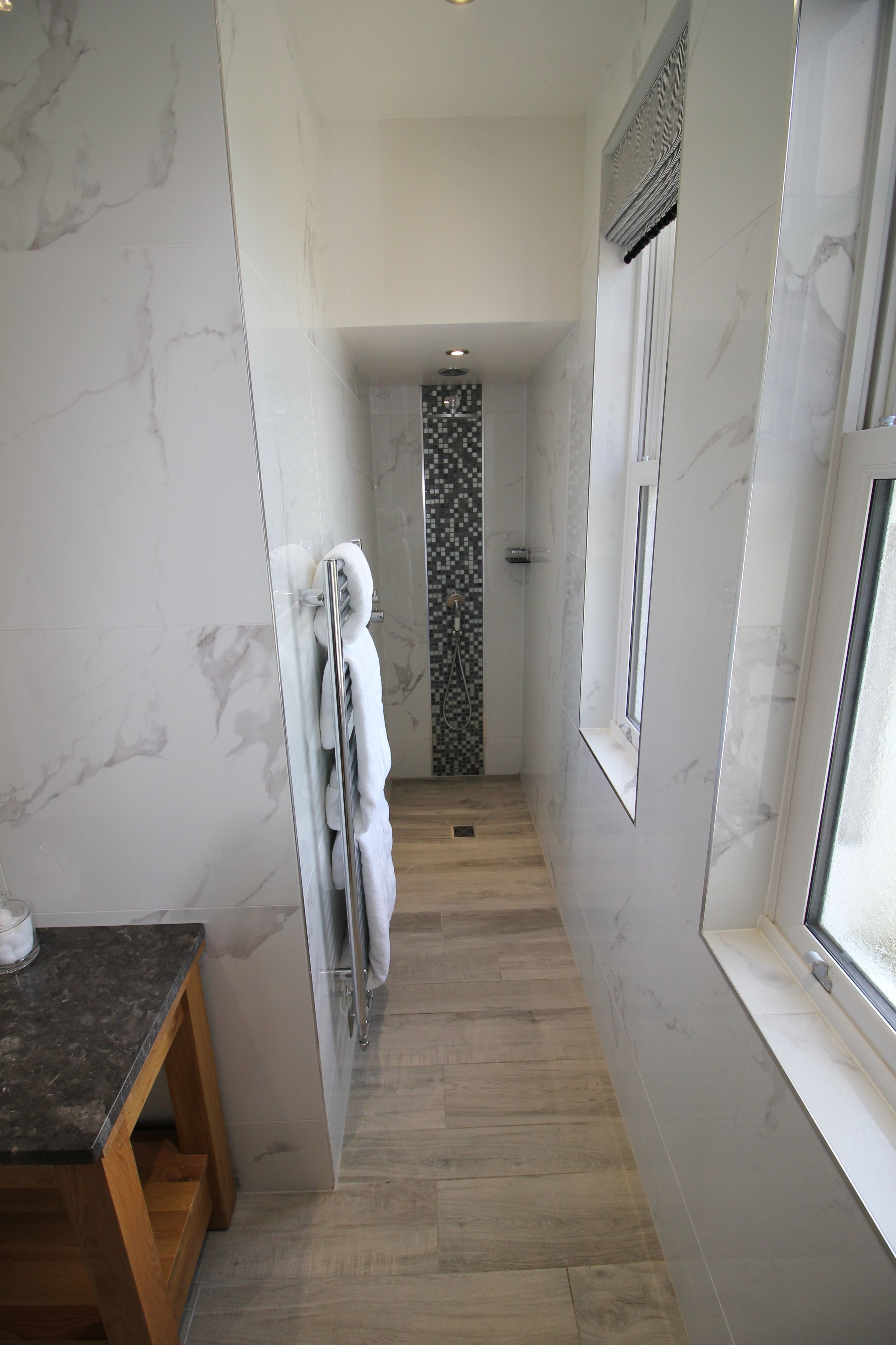 A narrow hallway with a glass shower door, a towel rack, and a window with a view.