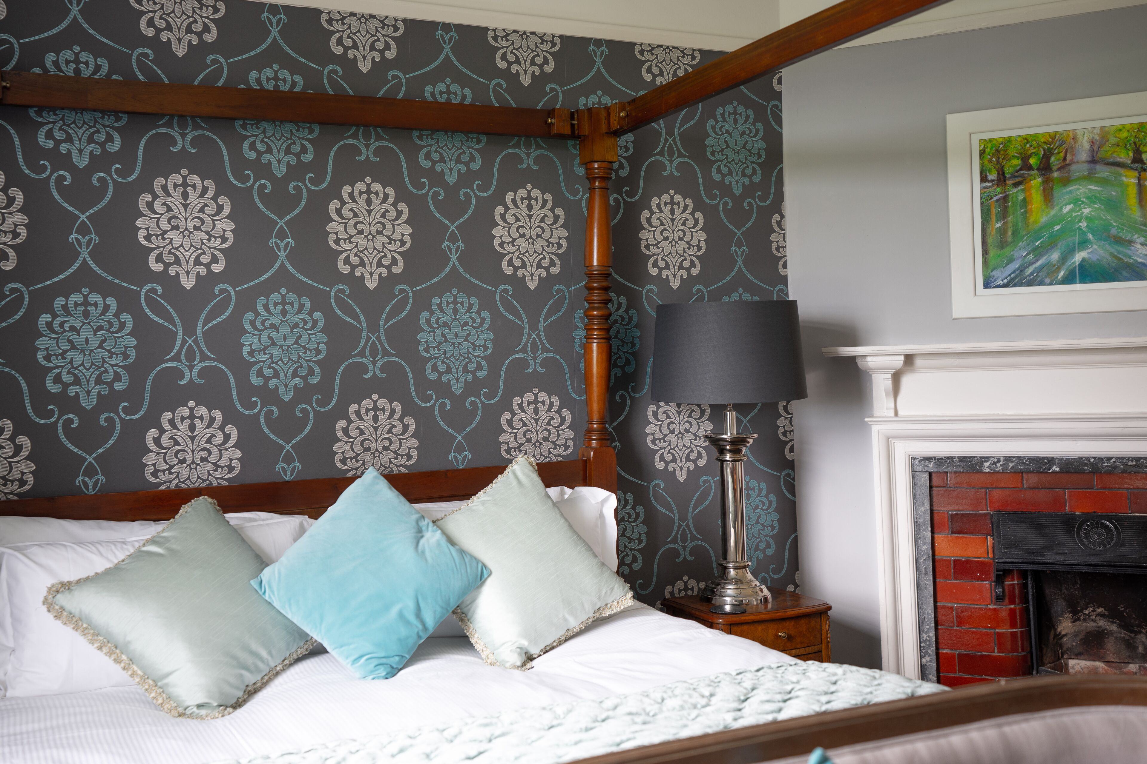 A bedroom with a four-poster bed, a fireplace, and a patterned wallpaper.