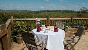 A wooden deck with a round table set for a meal, surrounded by chairs, overlooking a green landscape. - The Dower House Hotel (Lyme Regis)