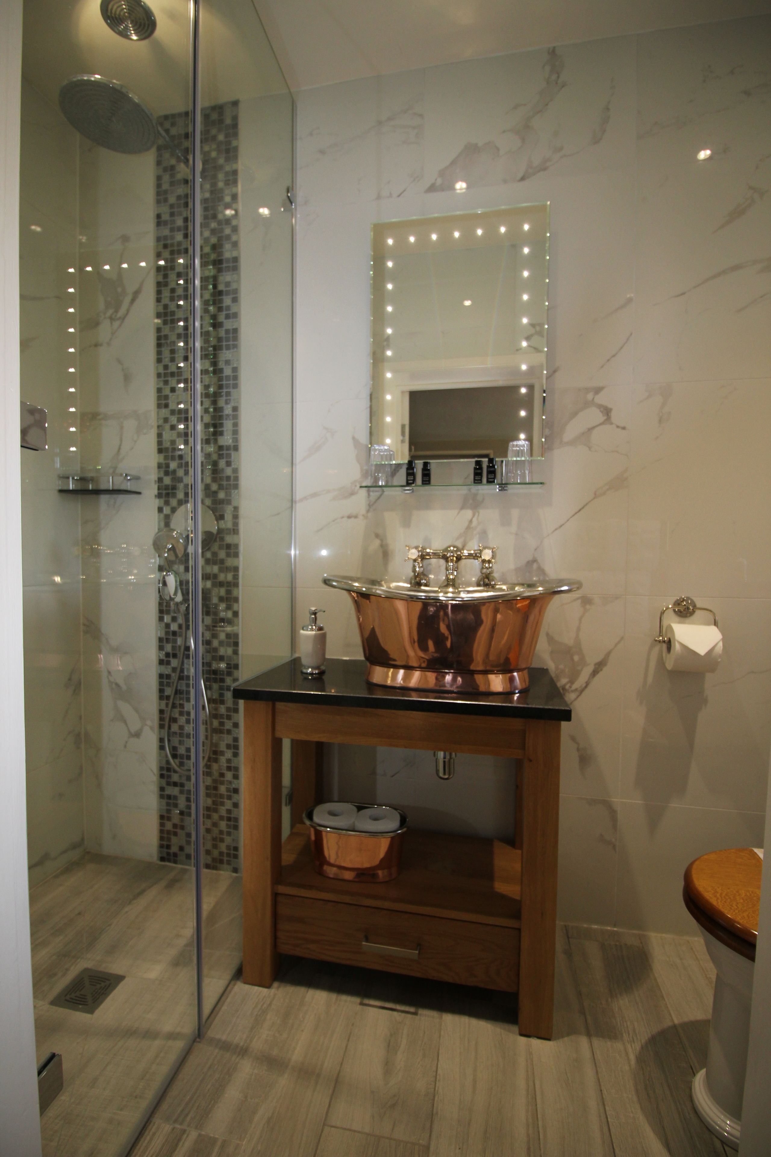 Une salle de bain dotée d’une douche à parois de verre, d’un évier en cuivre et d’un mur recouvert de carreaux de marbre.