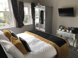 Un dormitorio ordenado con cama, armario, escritorio con artículos para preparar café y televisor en la pared.