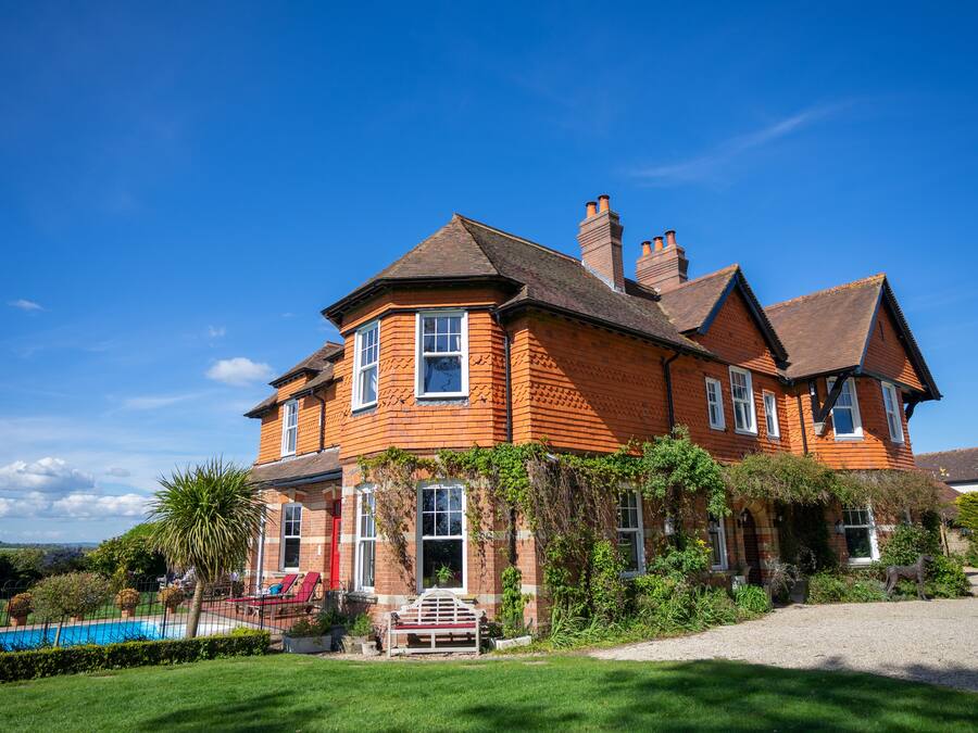 A large brick house with a swimming pool, surrounded by a well-maintained lawn and garden.