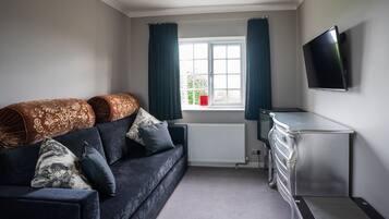 A modern living room with a dark blue sofa, patterned cushions, a flat-screen TV, and a dresser.