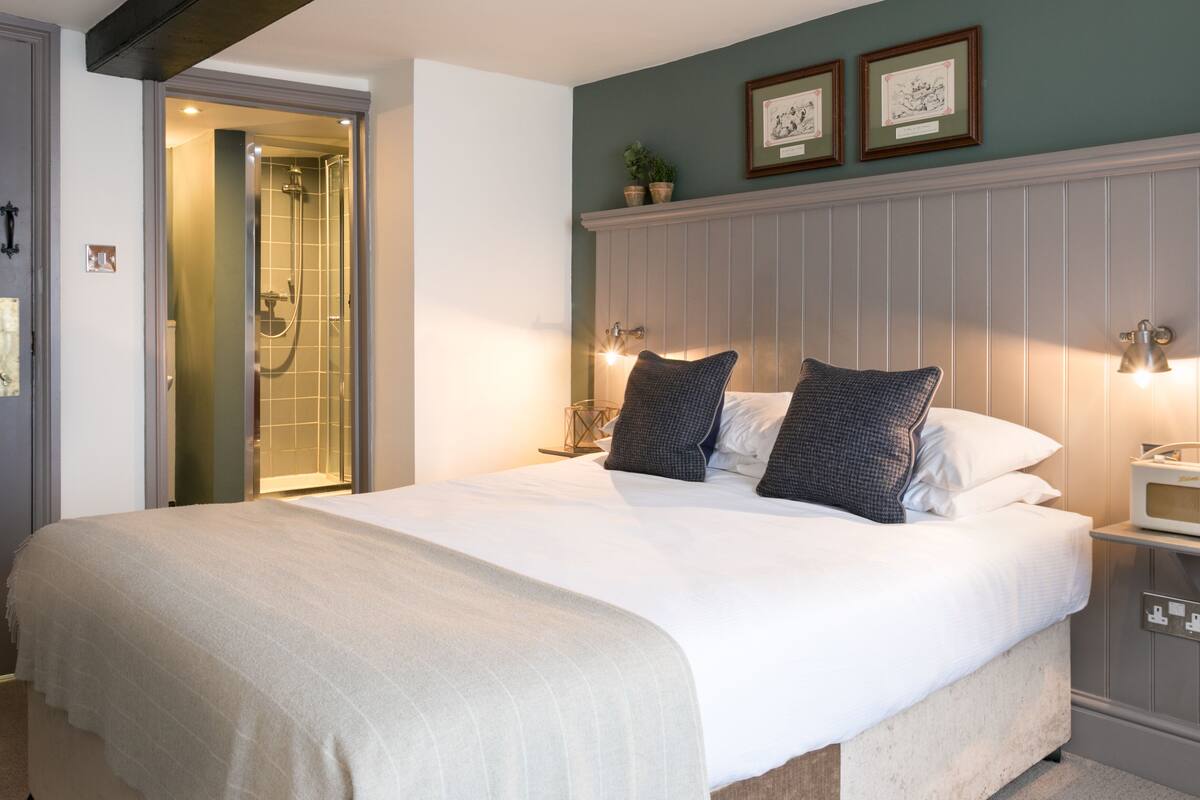 A neatly made bed with white linens and two pillows, a bedside table with a lamp, and a framed picture above the bed.