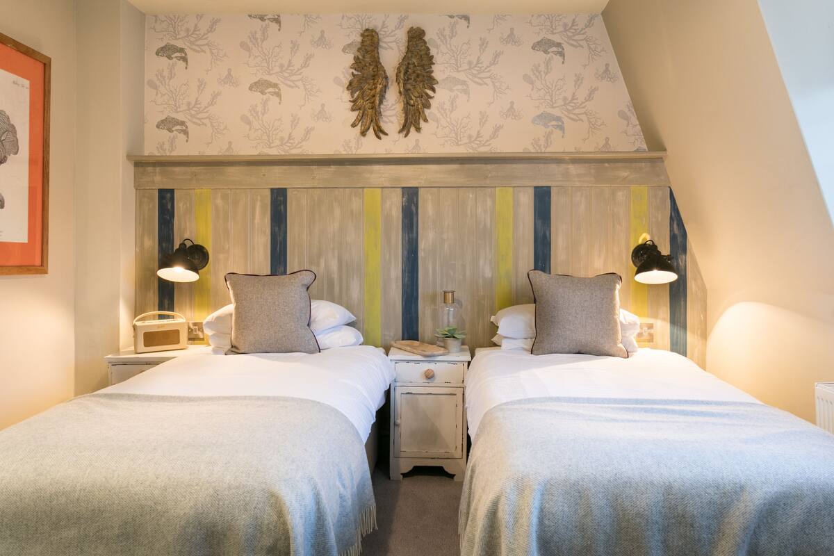 A twin bedroom with two beds, bedside tables, lamps, and a decorative wall panel.