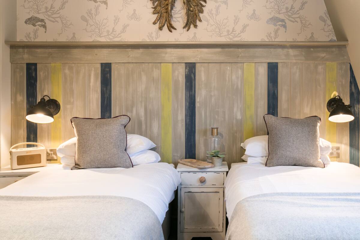A hotel room with two beds, a nightstand with a lamp, a radio, and a decorative wall panel.