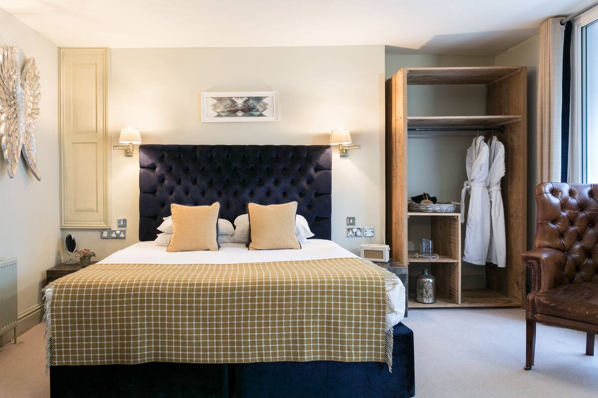 A bedroom with a large bed, two bedside lamps, a wooden wardrobe, and a leather armchair.