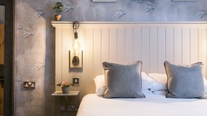 A neatly made bed with two pillows, a bedside table with a plant, and a wall with a bird mural. - Angel and Blue Pig (Lymington)
