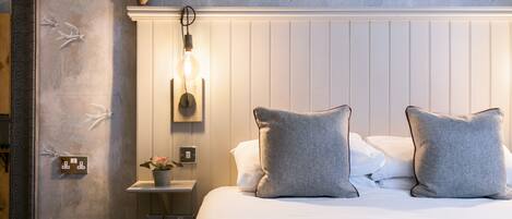 A neatly made bed with two pillows, a bedside table with a plant, and a wall with a bird mural.