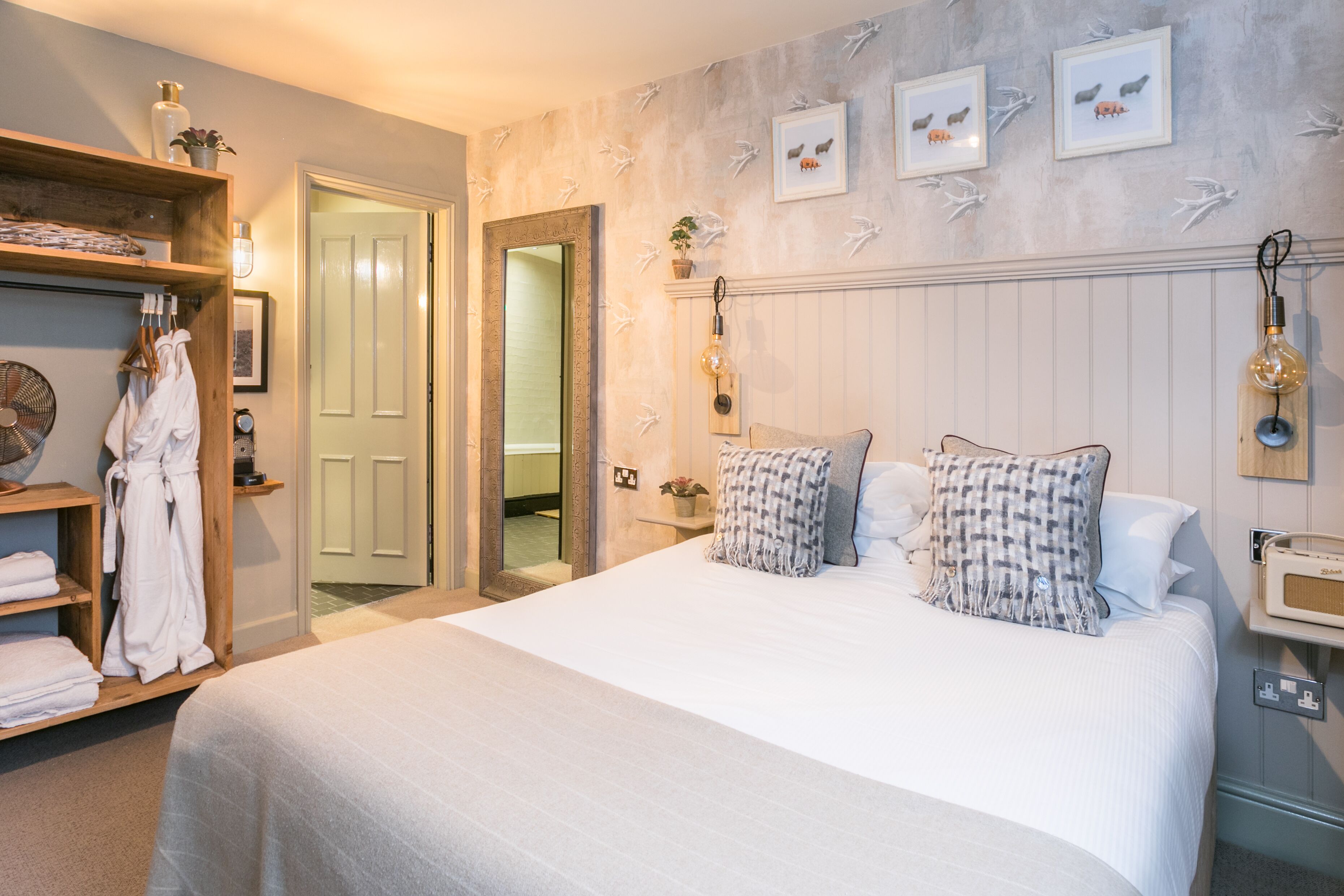 Habitación de hotel con una cama grande, un armario de madera, un espejo y una pared con cuadros.