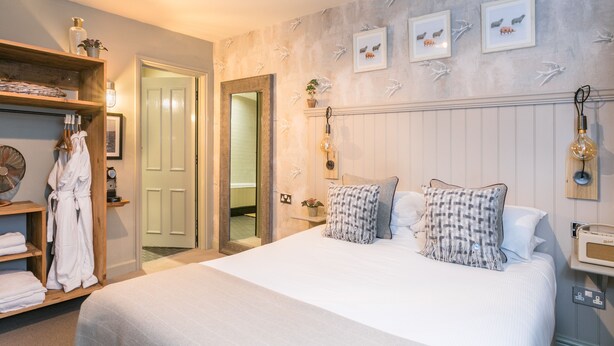 A hotel room with a large bed, a wooden wardrobe, a mirror, and a wall with framed pictures. - Angel and Blue Pig (Lymington)