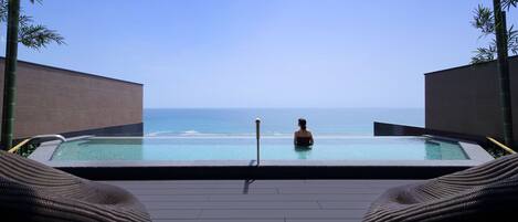 A pool with a view of the ocean, surrounded by bamboo plants and wicker lounge chairs.