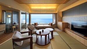 A modern hotel room with a large TV, comfortable seating, a dining area, and a view of the sea. - Kamogawakan (Kamogawa)