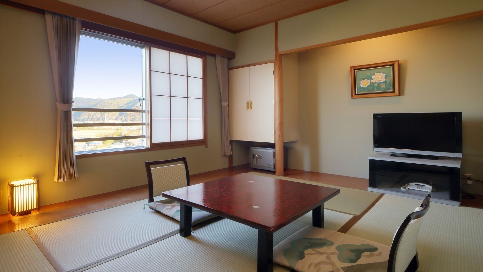 Ein Zimmer mit Tatami-Böden, einem Holztisch, einem Fernseher und Bergblick.