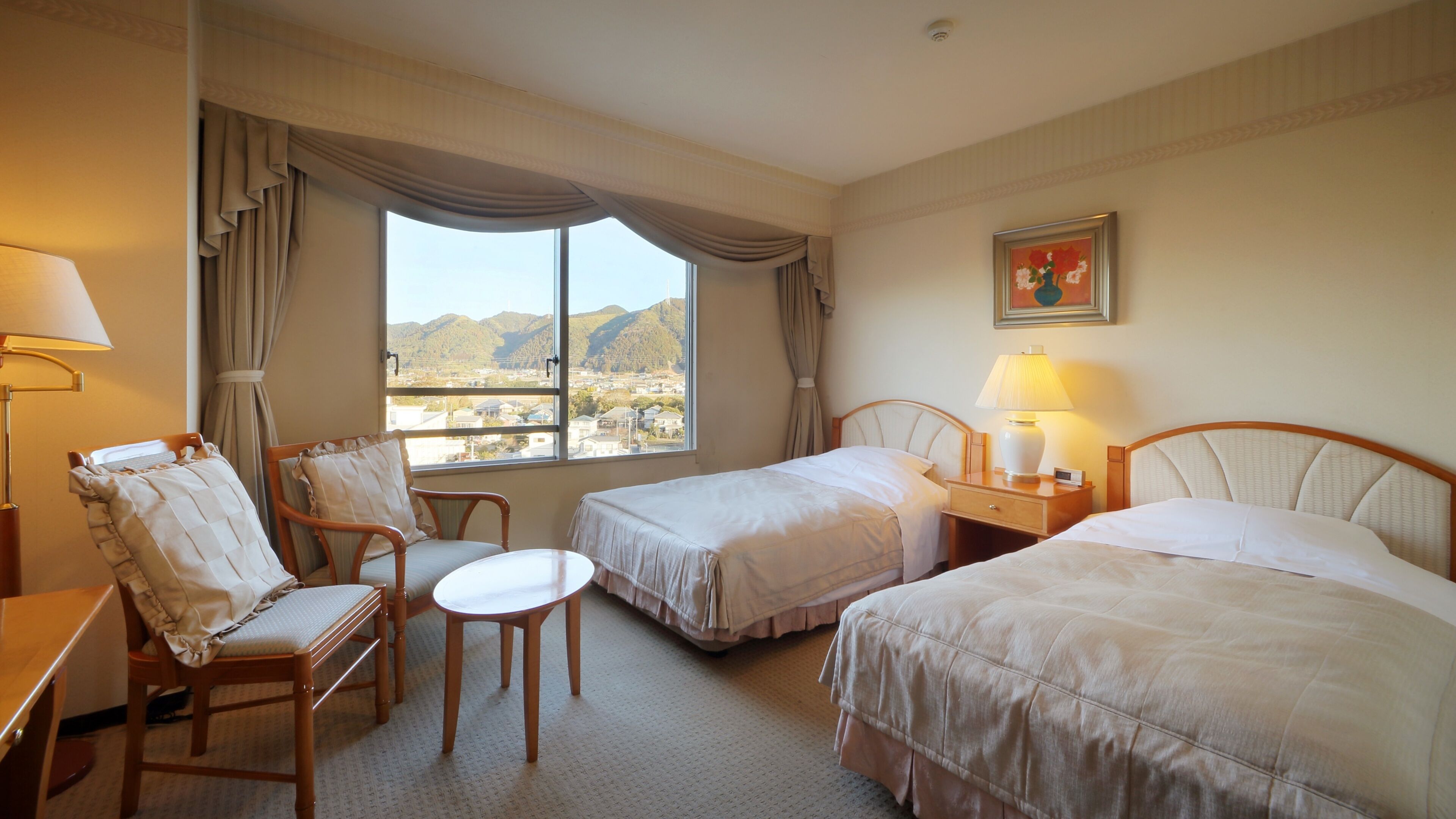 A hotel room with two beds, a chair, a small table, and a lamp.
