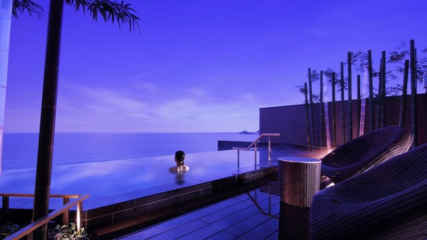 A serene infinity pool with a view of the ocean, surrounded by bamboo and lounge chairs. - Kamogawakan (Kamogawa)