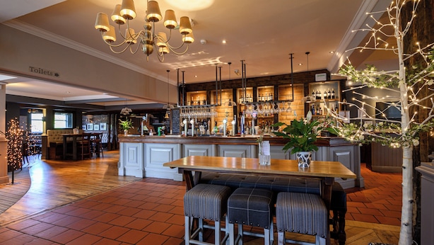 A bar area with a wooden counter, stools, and a chandelier. - White Rabbit Hotel by Chef and Brewer Collection (Lyndhurst)