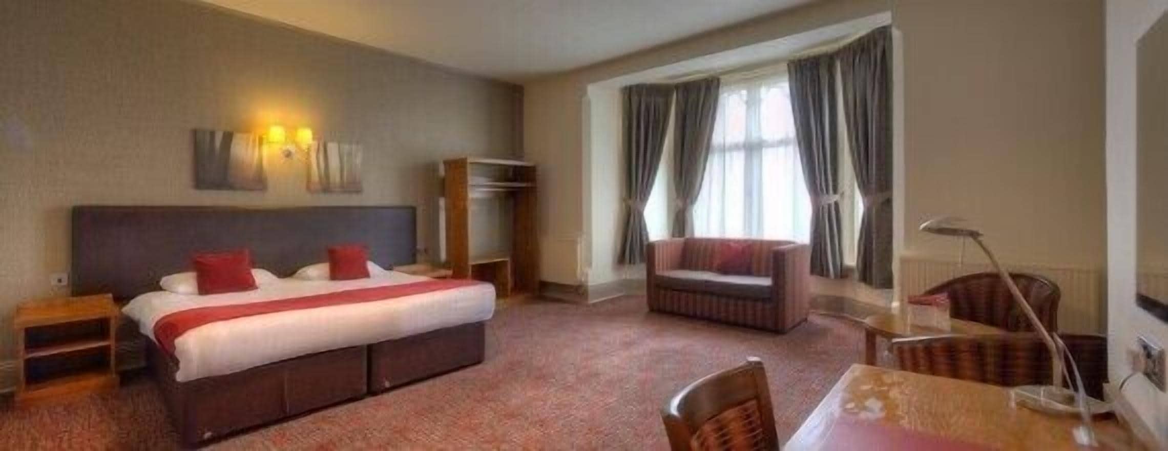 A hotel room with a bed, a chair, a table, and a lamp.