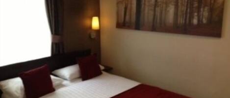 A hotel room with a bed, a painting on the wall, and a window with curtains.