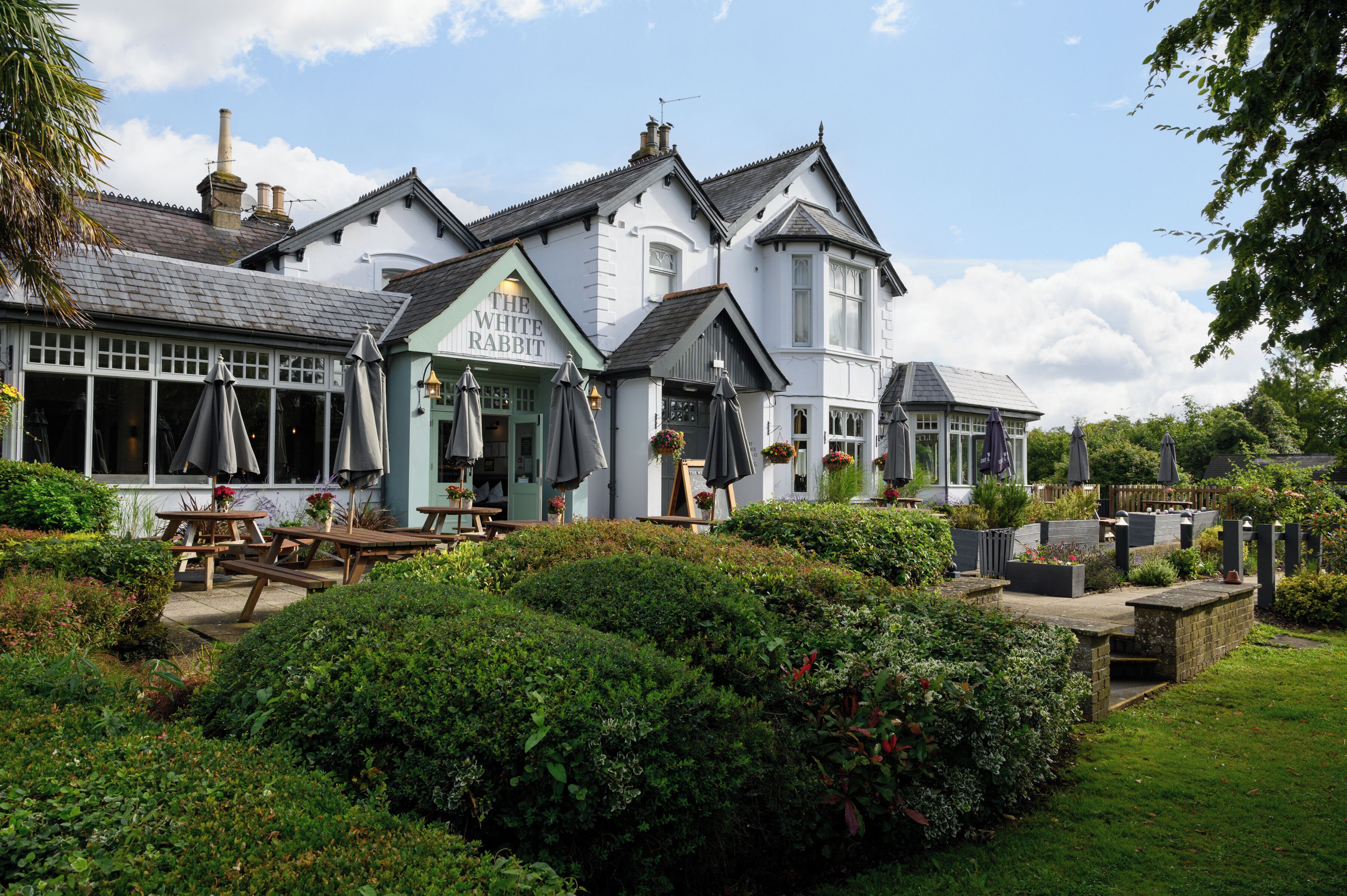 A traditional pub with outdoor seating, a well-maintained garden, and a classic architectural style.