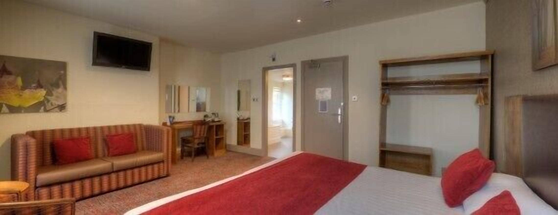 A hotel room with a bed, a sofa, a desk, and a television.