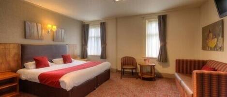 A hotel room with a bed, a small table, a chair, and a sofa.