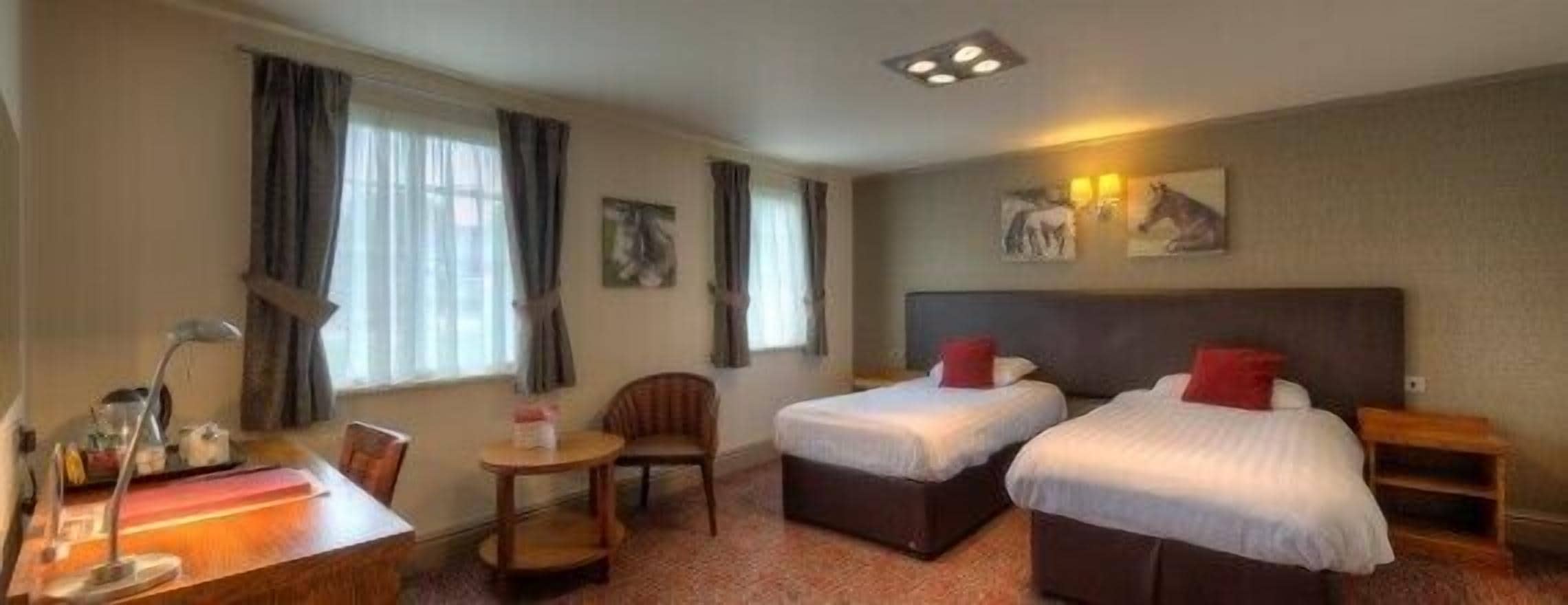 Habitación de hotel con dos camas individuales, un escritorio con silla, una mesita y una ventana con cortinas.