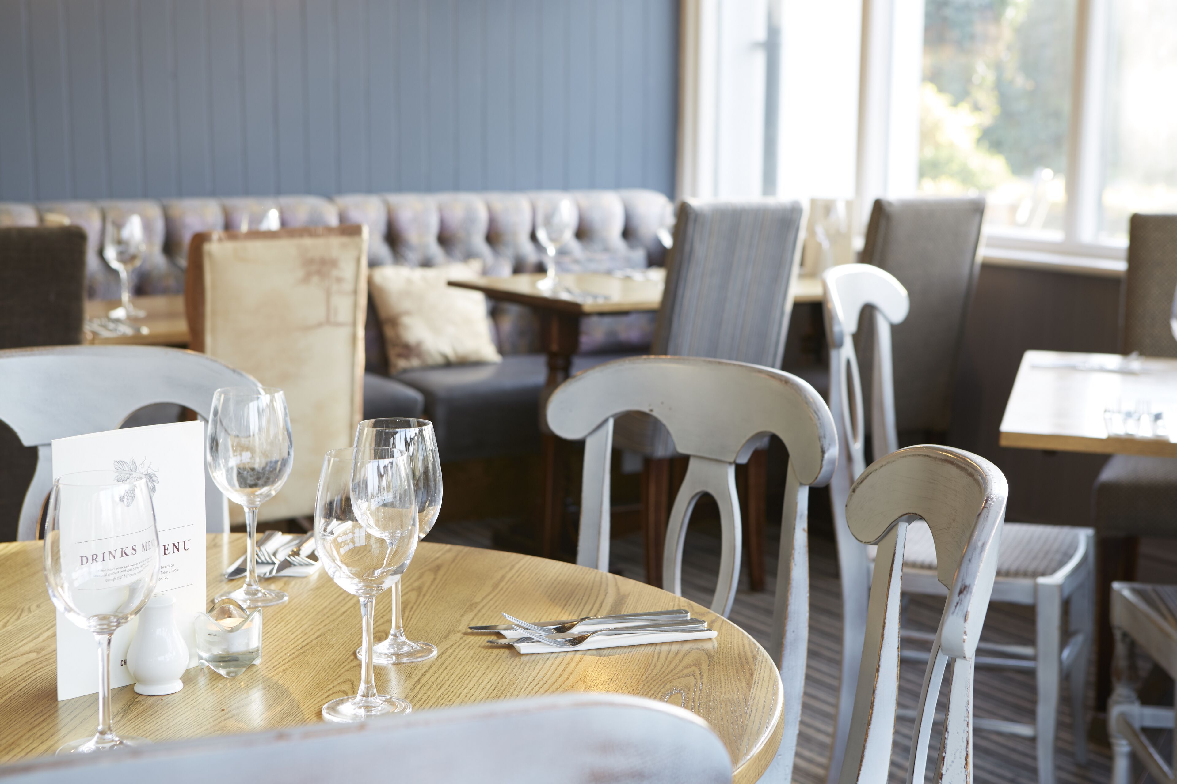 Een restaurantinterieur met een houten eettafel, een menukaart en wijnglazen.