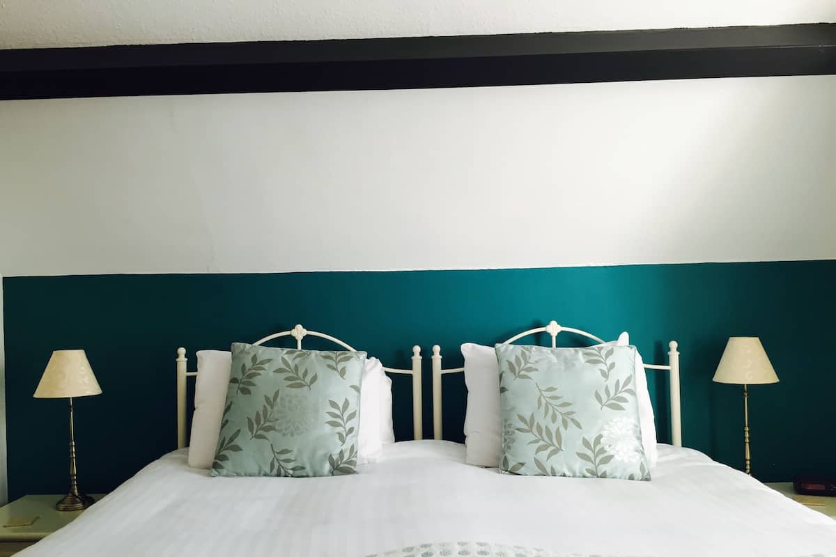 A neatly made bed with a white and light blue patterned bedspread, two matching pillows with a leaf pattern, and a teal headboard.
