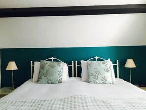 A neatly made bed with a white and light blue patterned bedspread, two matching pillows with a leaf pattern, and a teal headboard. - Longmead House (Lynton)