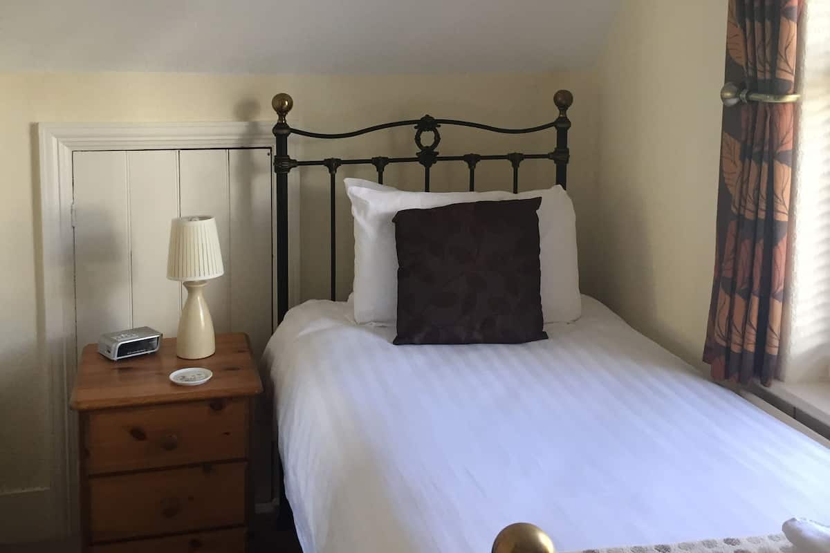 A bedroom with a bed, a nightstand, a lamp, and a window with curtains.