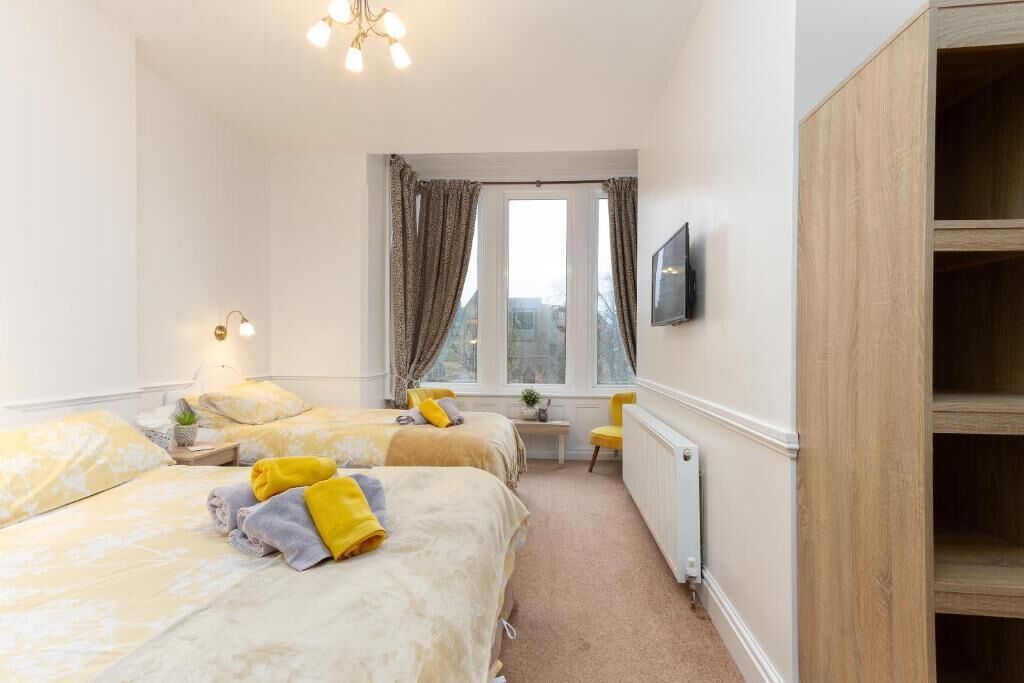 A hotel room with two beds, a small table, a chair, a radiator, and a TV mounted on the wall.