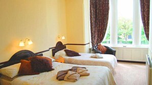 A hotel room with two beds, a window with curtains, and a lamp on the wall. - The Hollingworth (Lytham St. Anne's)
