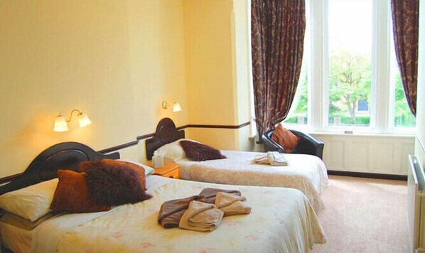 Quarto de hotel com duas camas, uma janela com cortinas e um abajur na parede.