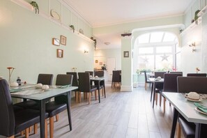A dining area with multiple tables and chairs, a kitchen in the background, and a large window with star decorations. - The Hollingworth (Lytham St. Anne's)