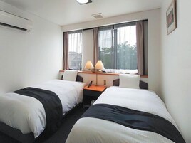 Habitación de hotel con dos camas, un escritorio con lámpara y ventana con cortinas.