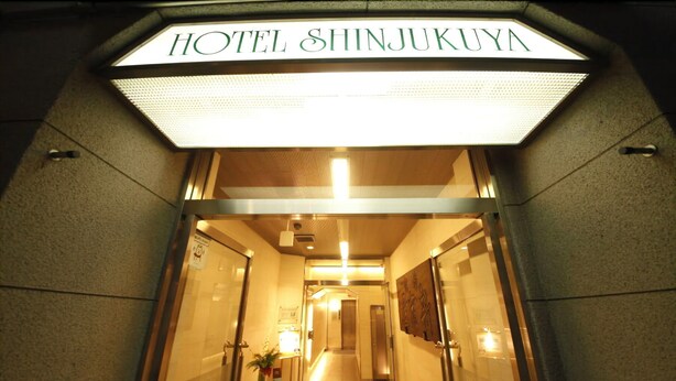 The entrance to Hotel Shinjukuya with a bright overhead sign, a reception desk, and a hallway leading to elevators. - Hotel Shinjukuya (Machida)