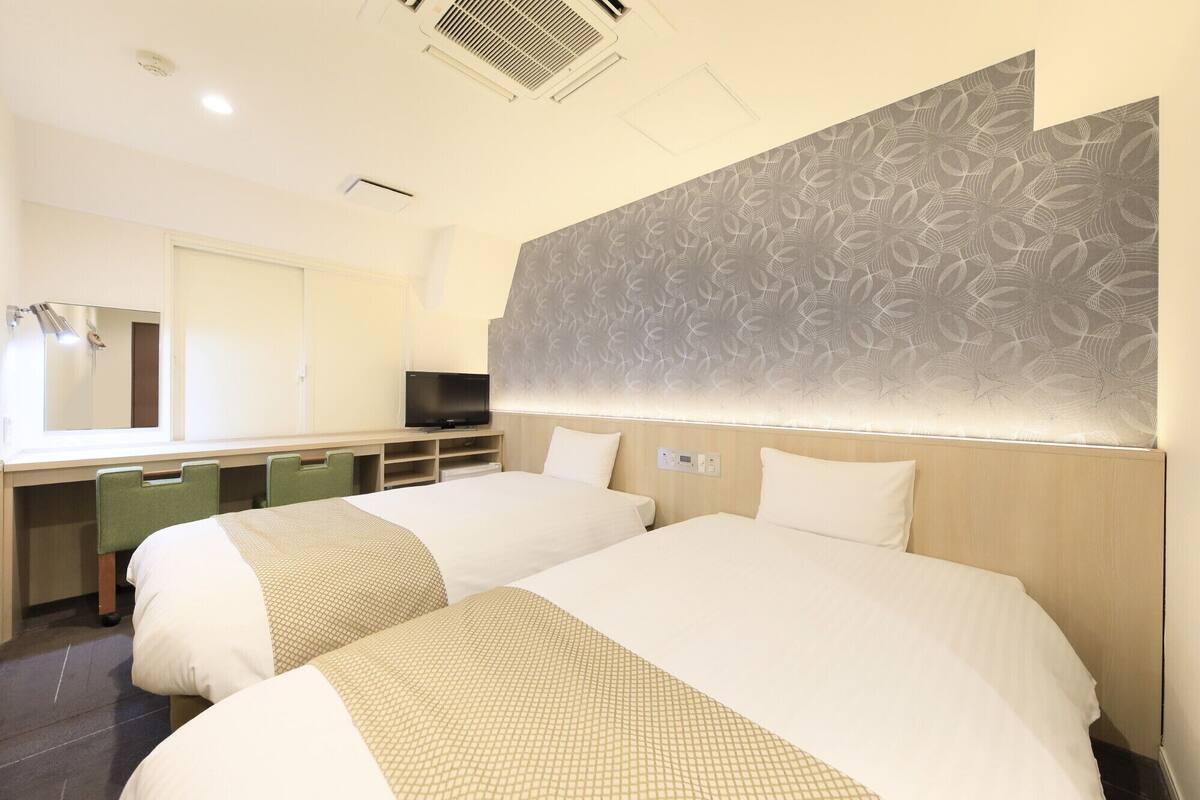 A hotel room with two beds, a desk with a flat-screen TV, a mirror, and a patterned wall.
