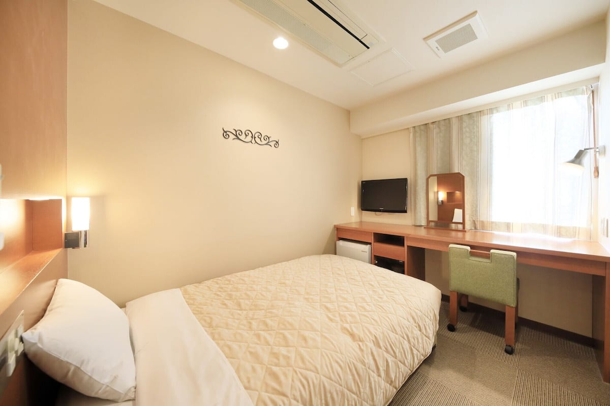 Una habitación de hotel con cama, escritorio, televisor y espejo.