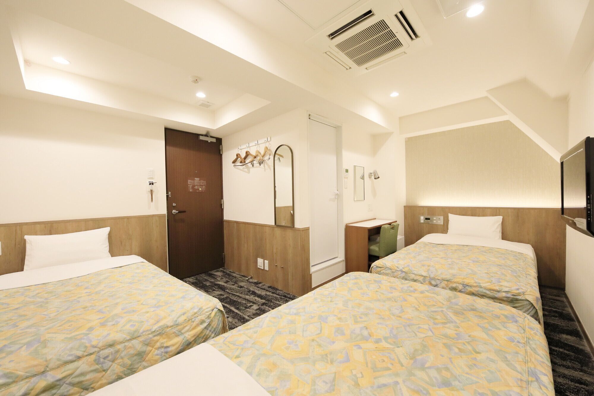 A hotel room with two beds, a bathroom, a mirror, and a TV.