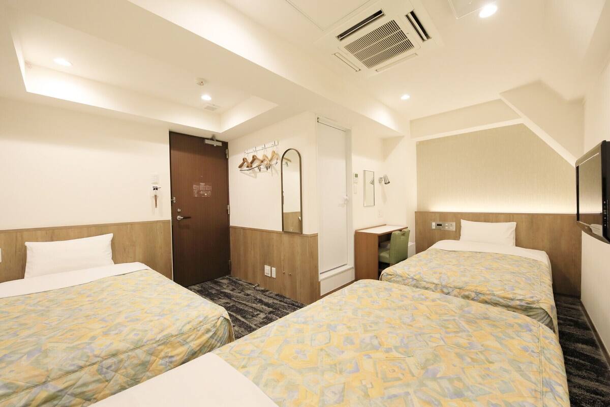 A hotel room with two beds, a bathroom, a mirror, and a TV.