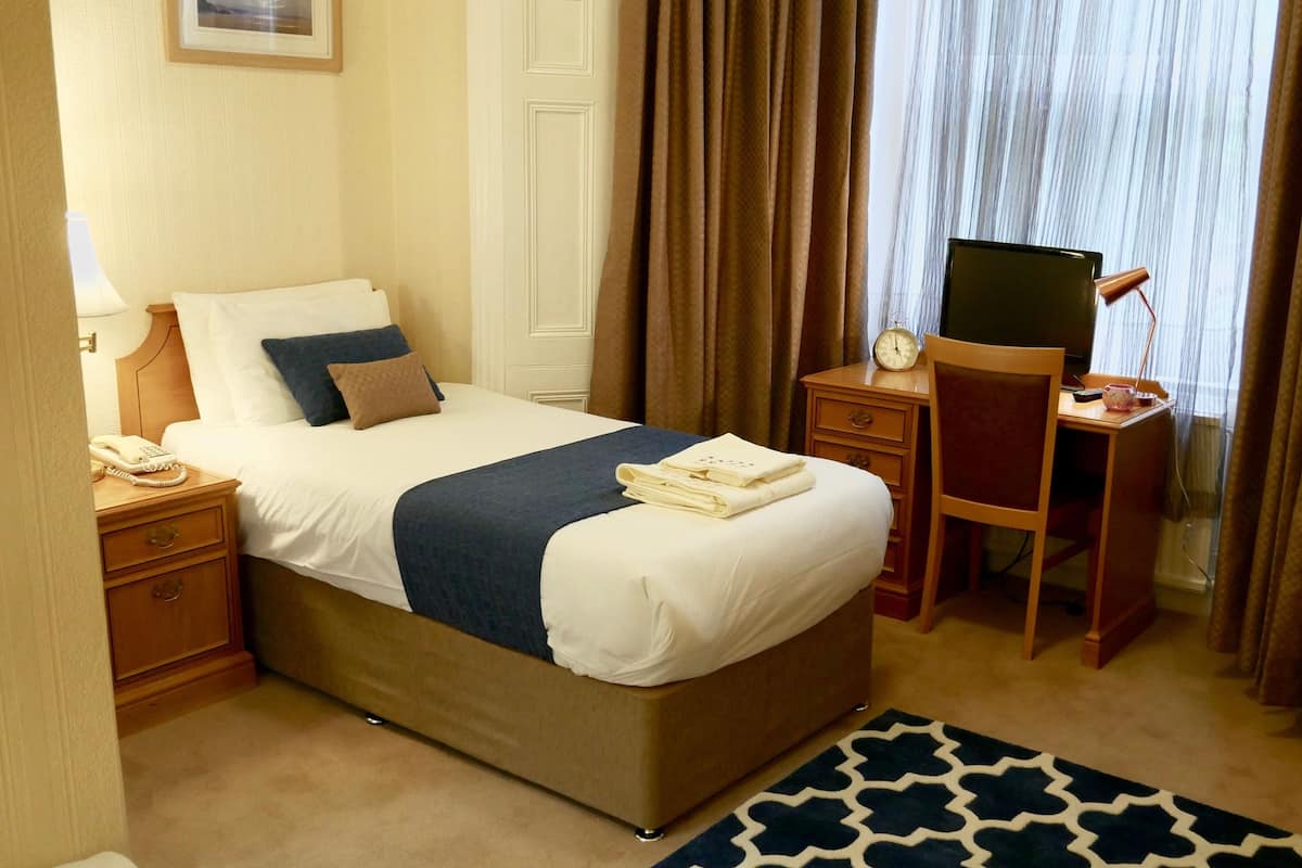 A hotel room with a bed, a desk with a computer, a chair, a telephone, and a clock.