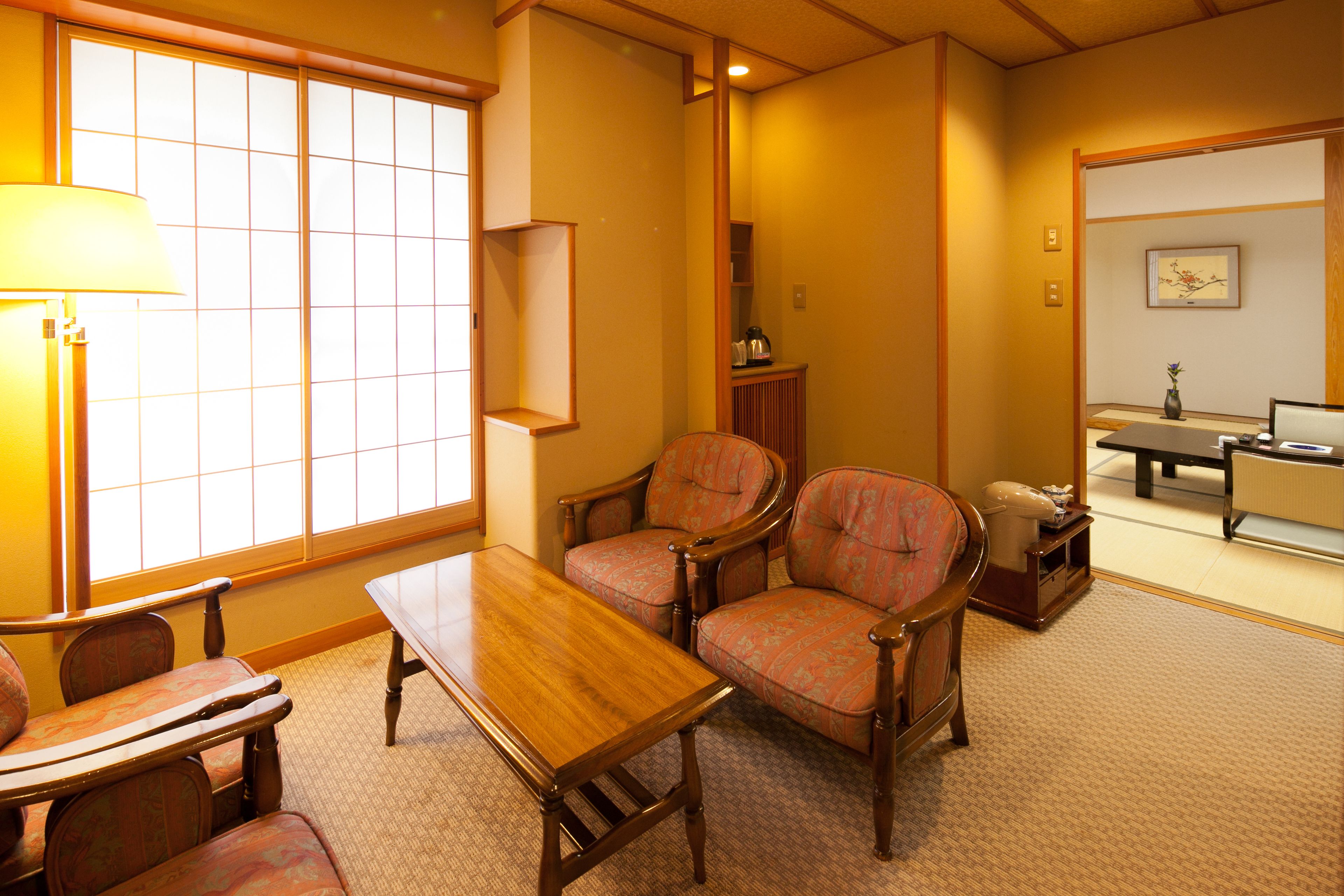 Una habitación de estilo japonés tradicional con suelo de tatami, una mesa baja, dos sillas estampadas, un armario y una puerta corredera.