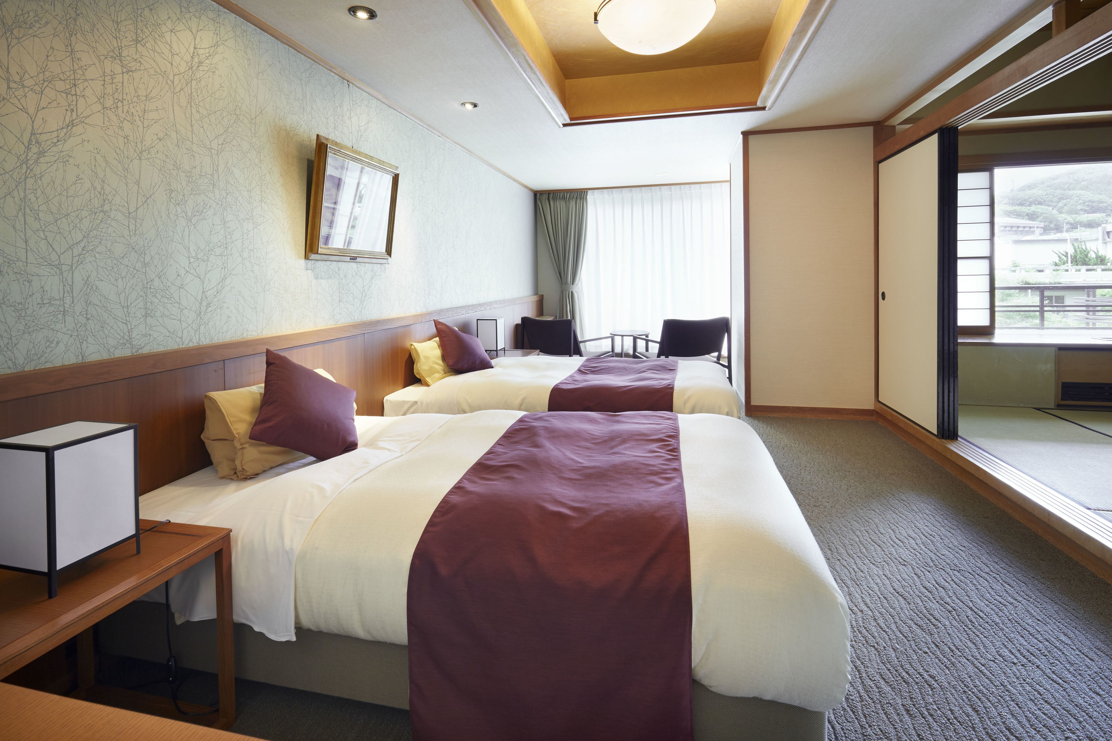 A hotel room with two beds, a desk, a chair, and a large window with a view.
