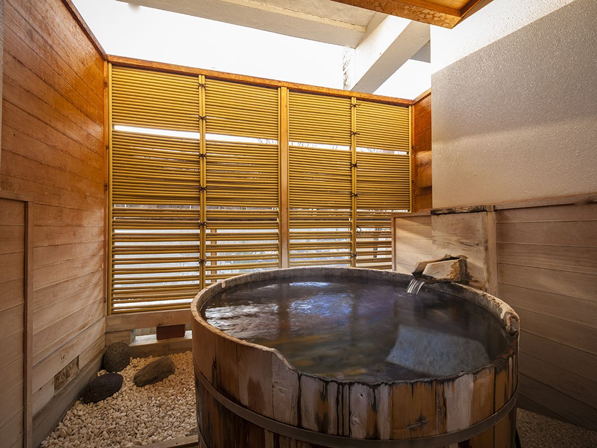 Uma sauna de madeira com uma banheira redonda grande, paredes de madeira e um painel de bambu.