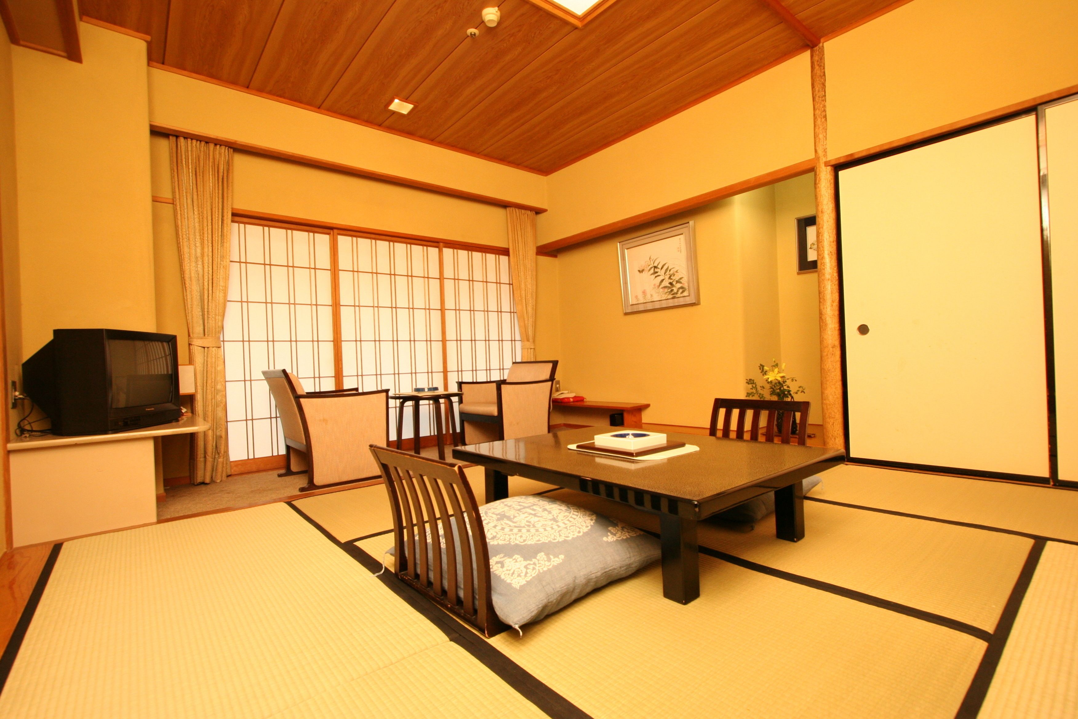 Una habitación japonesa tradicional con suelo de tatami, una mesa baja y un televisor sobre un soporte.